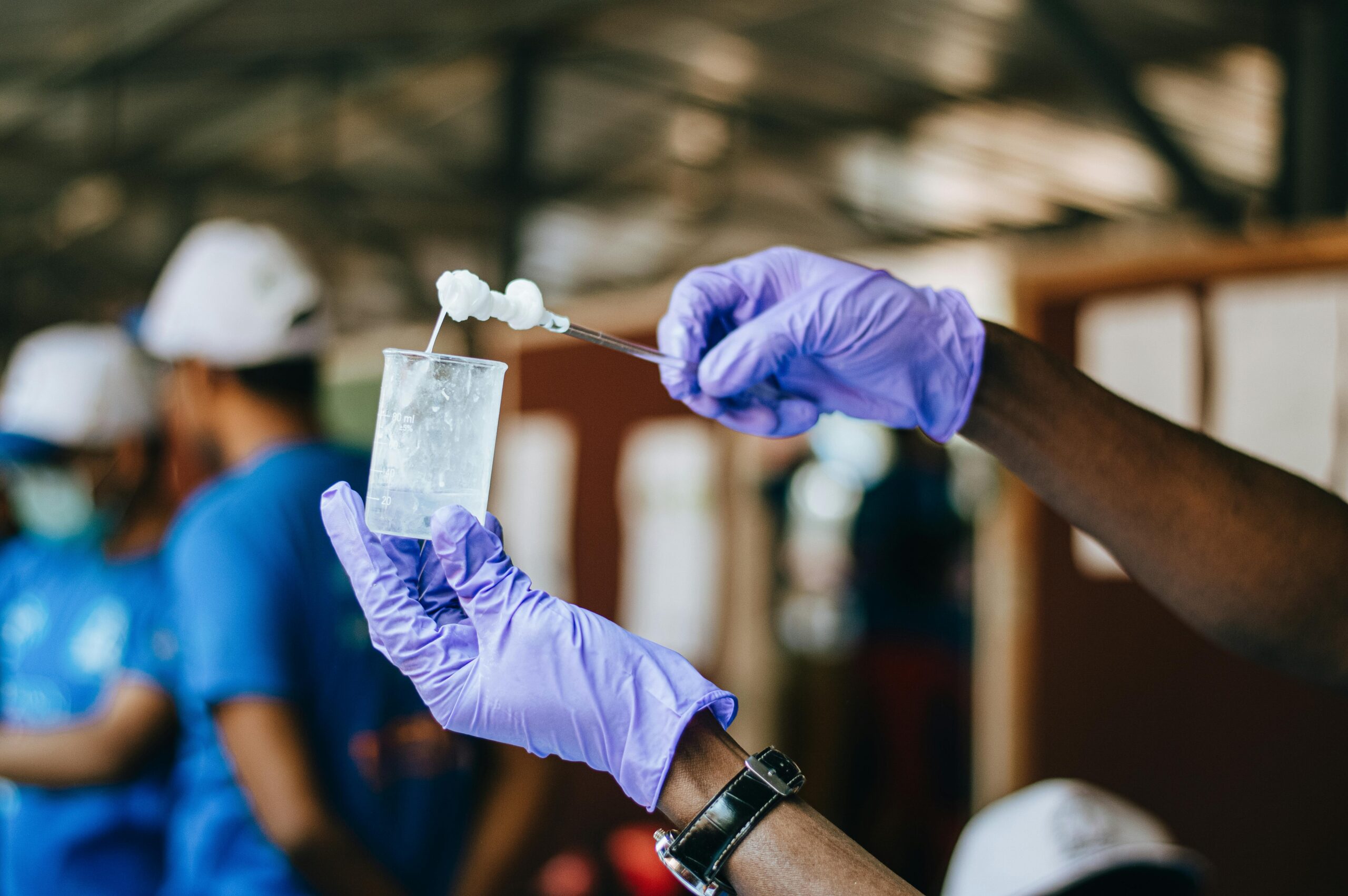 Multiracial crop anonymous people demonstrating flask and glass stick with chemical thick substance in laboratory in soft focus