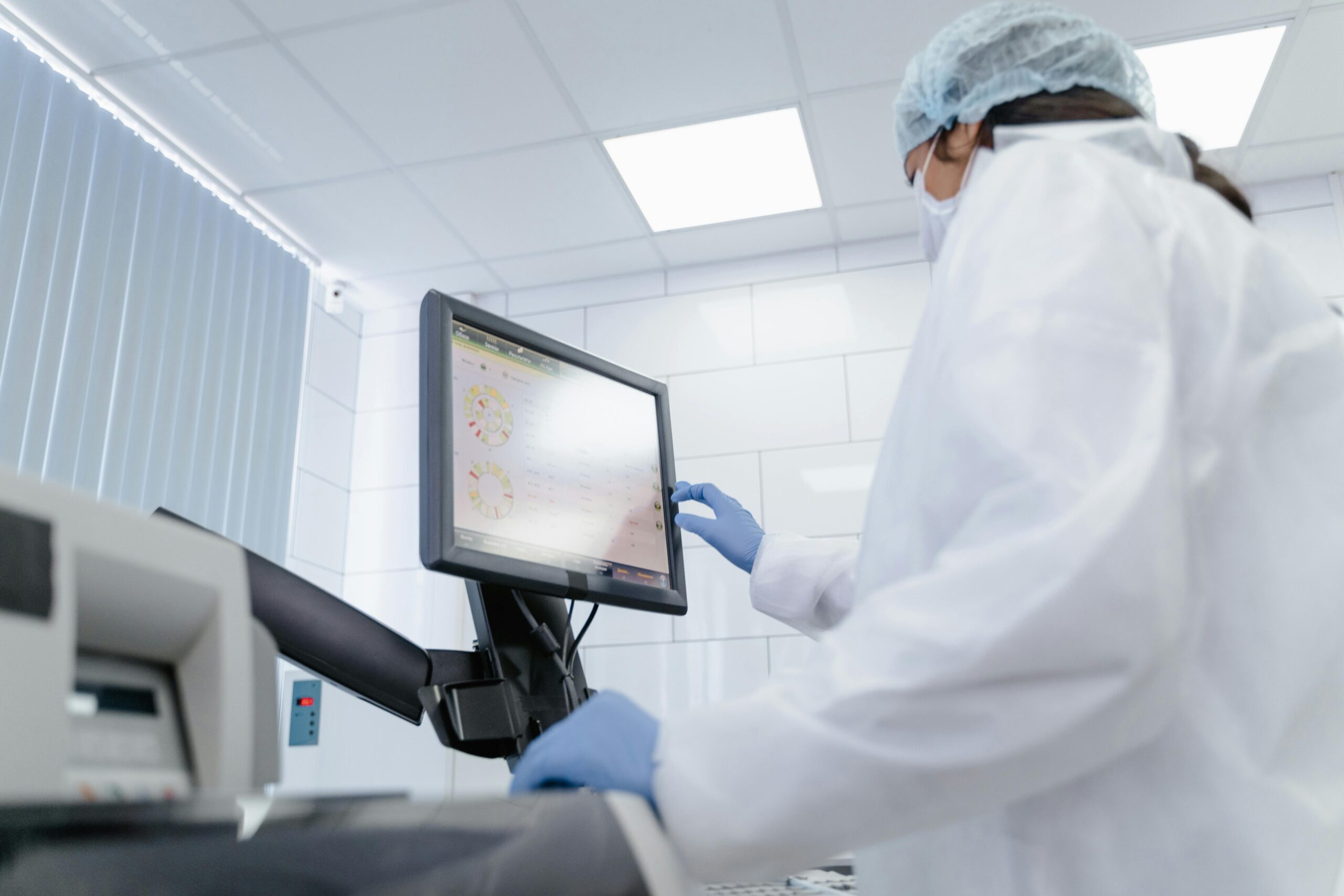 Woman in lab coat using touchscreen monitor in a modern laboratory setting.